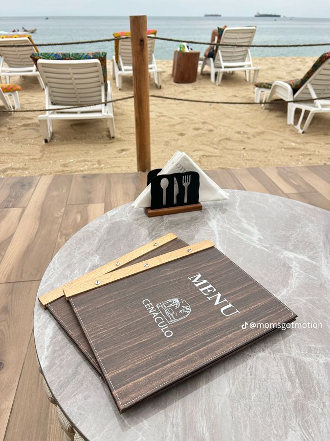Menu do Cenáculo numa mesa junto às espreguiçadeiras, com o mar ao fundo
