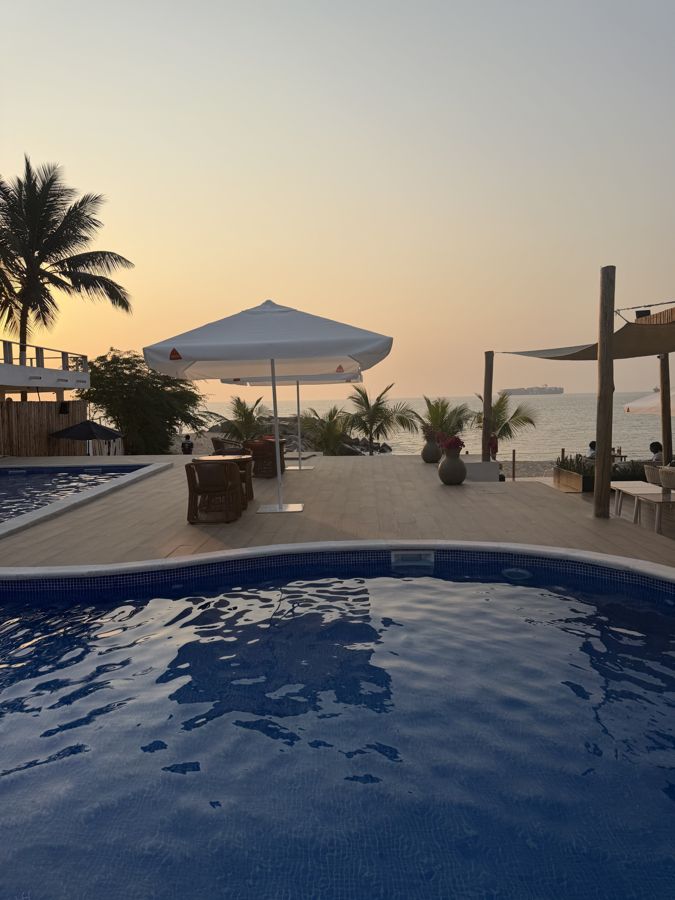 Piscina ao pôr-do-sol com chapéu branco e o mar em fundo